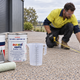 Tradesperson measuring an exposed aggregate driveway beside Dulux Avista Exposed Aggregate Sealer, Auseal sealer, a measuring jug and lambswool roller